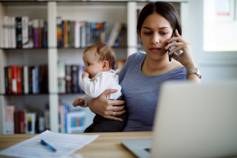 赤ちゃんを抱えながらパソコンに向かって電話をする母親
